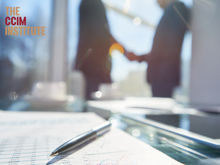 paperwork with two business people shaking hands in the background.