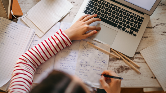 Woman in a striped shirt working on an online course with a laptop, notebook, and pencils.