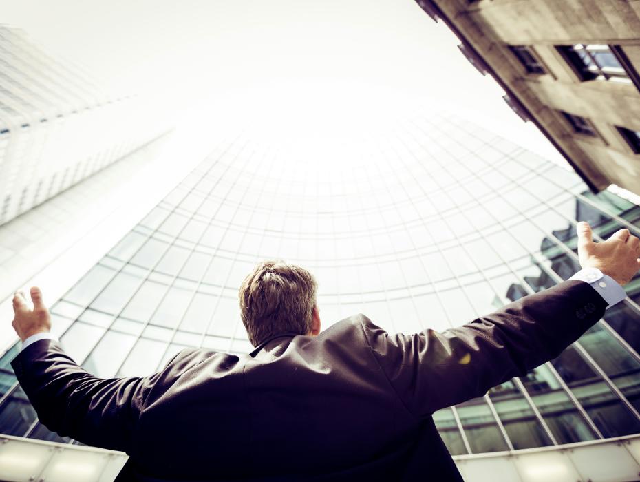 White male with blond hair raising his hands up to skyscrapers.