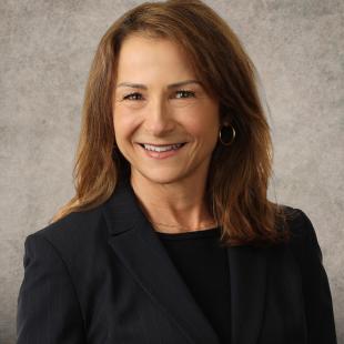 Caucasian woman with reddish brown shoulder length hair wearing a black blazer and shirt.