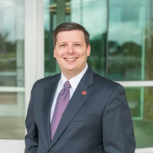 Caucasian man in dark suit with short brown hair.